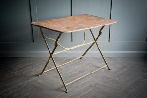 A French design bistro table in distressed metal with folding mechanism exhibiting rustic charm.