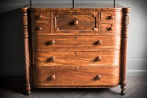 Large Scottish demi bow fronted chest made from rich mahogany with intricate carvings on pillars framing the piece.
